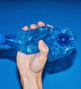 Hand squeezing plastic bottle on blue background. Zero waste and consumption reduction of plastic